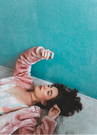 a person wearing pink fur jacket lying on a carpet floor look up at her hand