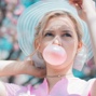 headshot of a person wearing a hat blowing a bubble with bubblegum